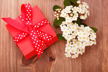 Red gift box tied red ribbon and flowers on wooden background