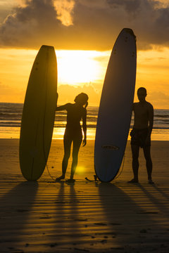 surfers with surfboard on the beach at sunset