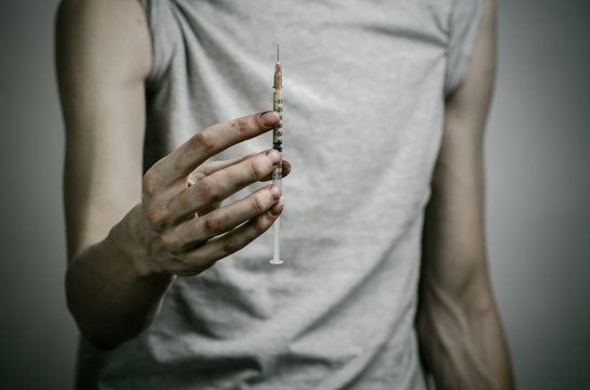 skinny dirty addict holding a syringe with a drug in studio