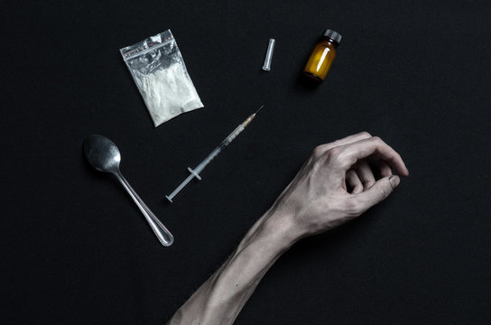 hand addict lies on a dark table and around it are drugs