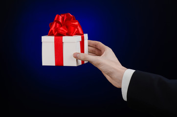 man in a black suit holding gift wrapped in white box in studio