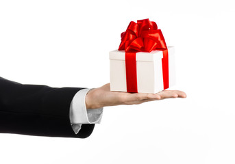 man in a black suit holding gift wrapped in white box in studio