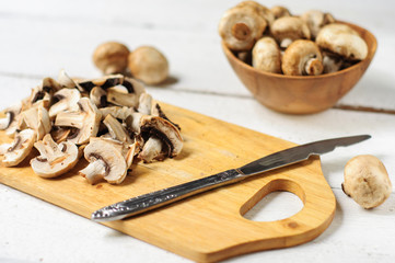 Obraz na płótnie Canvas Sliced champignons on board and wooden bowl