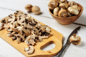 Fototapeta na wymiar Sliced champignons on board and wooden bowl