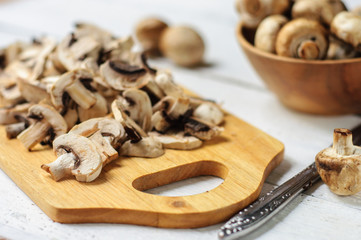 Fototapeta na wymiar Sliced champignons on board and wooden bowl