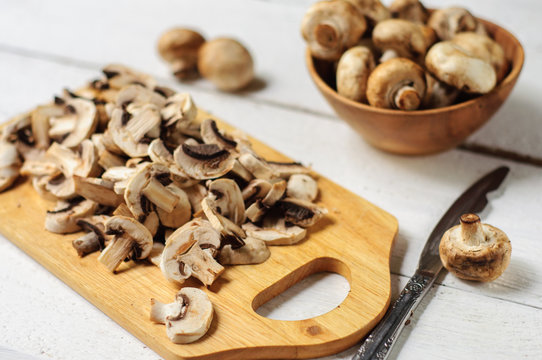 Sliced champignons on board and wooden bowl