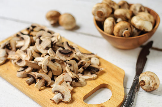 Sliced champignons on board and wooden bowl
