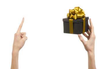 hand holding a gift wrapped in a black box with gold ribbon
