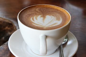 Hot cappuccino in white cup on wooden table.