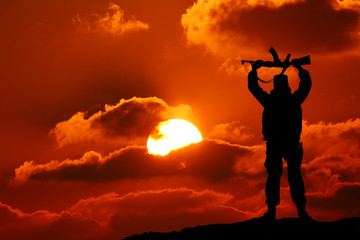 Silhouette shot of soldier holding gun with colorful sky 
