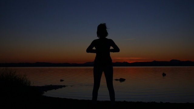 Young woman doing exercises at sunset