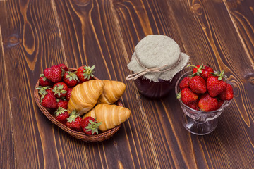 Strawberries and croissant on a wooden brown background