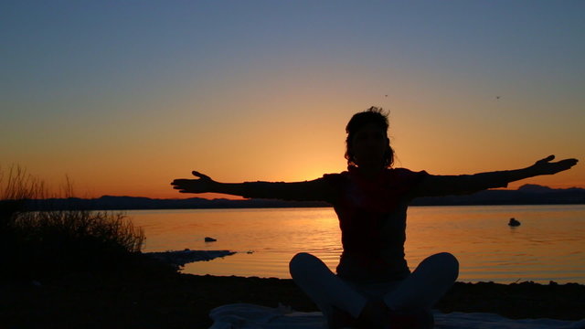 Silhouette of woman meditating at sunset