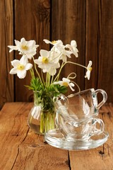 White anemones and two glass cups and saucers on wooden backgrou