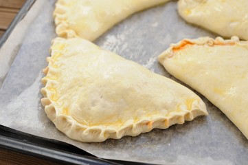Raw calzone pizzas on papered frying pan