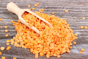 Heap of red lentil with spoon on wooden background