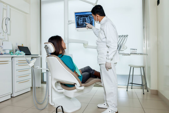 Asian dentist is showing X-ray on a screen to his patient