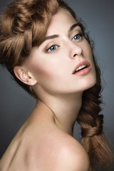 Fototapeta premium Beautiful girl with light make-up, perfect skin and hairstyle as a braid. Picture taken in the studio on a gray background