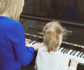 Woman teaching little girl to play the piano. Back view.