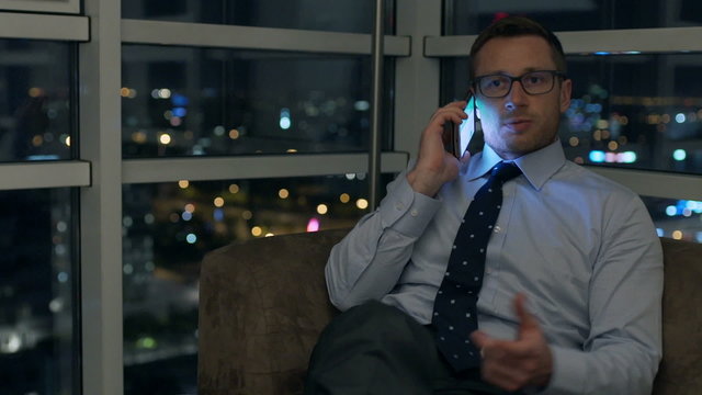 Businessman sitting on the sofa at night and talking on cellphone
