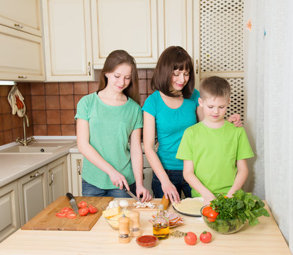 Teenager boy and girl with their mother cooking pizza at home.