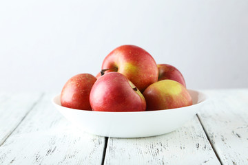 Apples in bowl on white wooden background