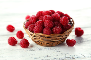 Raspberries in basket on white wooden background