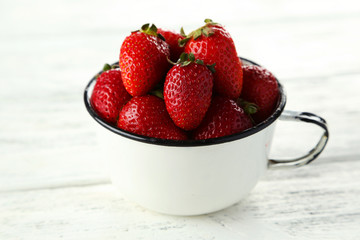 Strawberries in cup on white wooden background