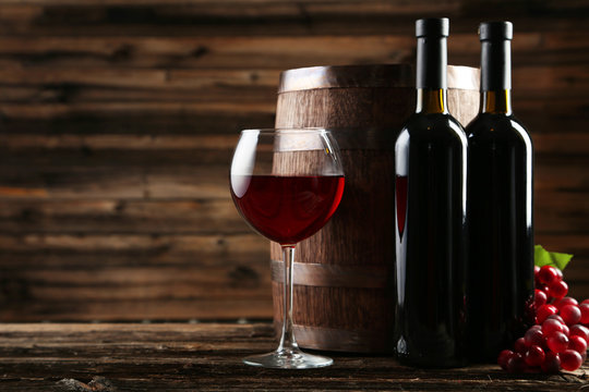 Red wine glass with bottle and barrel on brown wooden background