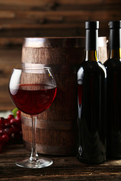 Red wine glass with bottle and barrel on grey wooden background