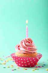 Tasty cupcake with candle on green background