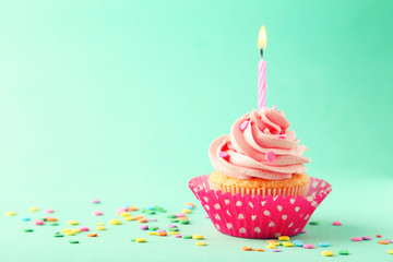 Tasty cupcake with candle on green background