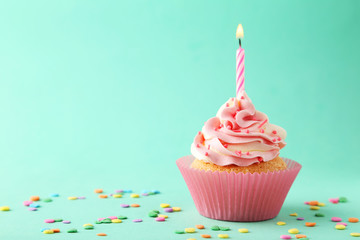 Tasty cupcake with candle on green background