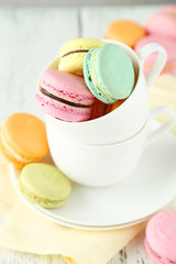 French colorful macarons in cup on white wooden background