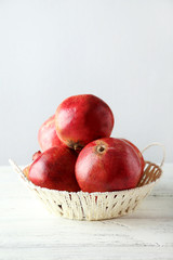 Fototapeta na wymiar Delicious pomegranate fruit in basket on white wooden background