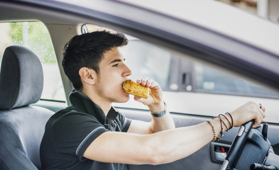 Young man driving his car while eating food
