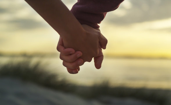 Couple holding hands on a beach at sunset