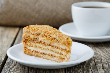 Tasty honey cake with cup of coffee on wooden background.