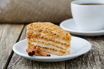 Tasty honey cake with cup of coffee on wooden background.