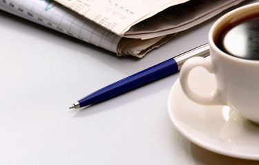 Cup of coffee, pen and newspapers on the desk