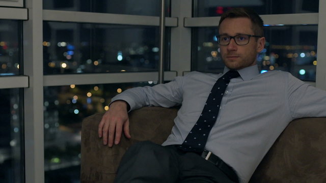 Tired businessman sitting on the sofa at night and resting
