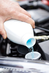 Close-Up Of Man Topping Up Windshield Washer Fluid In Car
