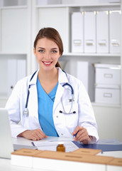 Fototapeta na wymiar Beautiful young smiling female doctor sitting at the desk and