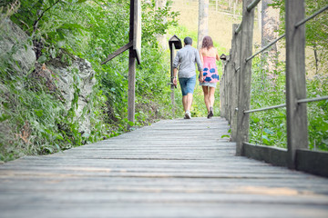 Low perspective of loving couple walking on a wooden bridge surrounded by the natural park of the...