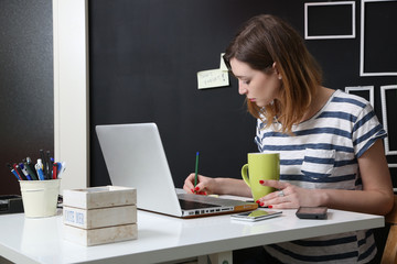 Young woman in front of laptop writing a note