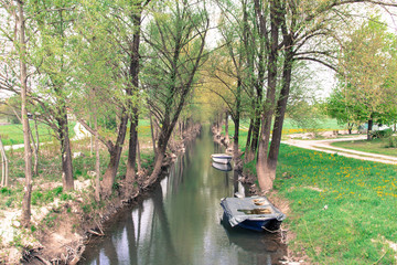 Rural channel with boats between trees and two country roads.