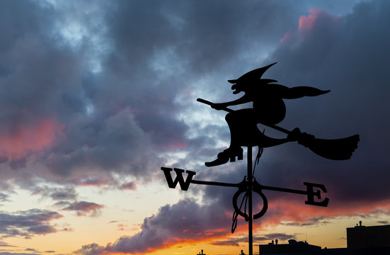 Silhouette of Halloween witch flying on broomstick above a city  
