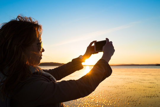 Woman taking selfie on a beach during sunset