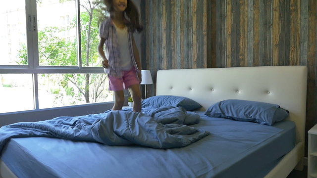 Slow motion of cute little Asian girl jumping on the bed