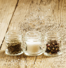 Spices: salt, pepper and herbs in small glass jar on a wooden ta